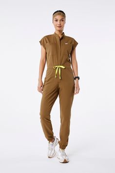 Why We Love ThisCasual and convenient. The FIONx™ Rafaela ScrubJumpsuit™ features nine pockets, a high rise waistband and gathered elastic cuffs for the best all-in-one option.

Model Fit Description
Model is 510' / Wearing XS

Total of nine pockets 
Two chest pockets 
Two hand pockets 
Two drop zipper pockets at waist 
Two back drop pockets 
One pen sleeve pocket
High rise waistband with adjustable drawcord
Badge loop at waistband
Back darts for shaping
Gathered elastic cuffs
Zippered front clo Figs Scrubs, Nurse Uniform, Back Drop, Awareness Ribbon, Current Styles, Awareness Ribbons, Model Fits, Scrub Tops, Anti Wrinkle