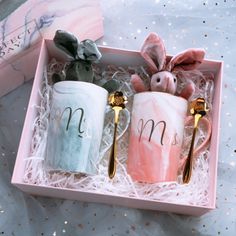 two coffee mugs with the letter m on them in a pink box next to a cactus