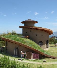 an unusual house in the middle of a field with grass growing on it's roof