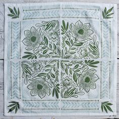 a white table cloth with green flowers and leaves in the center on a wooden surface