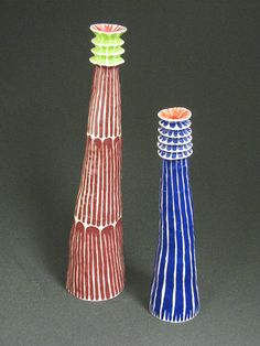 two colorful vases sitting next to each other on a black surface with white and red stripes