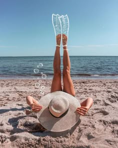 a woman laying on top of a sandy beach next to the ocean under a blue sky