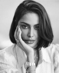 a black and white photo of a woman with her hand on her face, looking at the camera