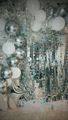 silver and white balloons are hanging on the wall next to a mirror with lights in it