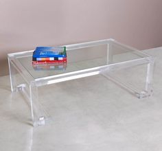 a clear glass coffee table with two books on the bottom and one book sitting on top