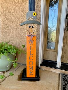 a welcome sign with a scarecrow's hat on it sitting in front of a door