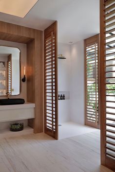 an open bathroom with wooden shutters and white counter top, along with a large mirror on the wall