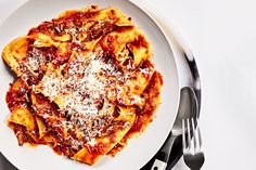 a white plate topped with pasta covered in sauce and parmesan cheese next to silverware