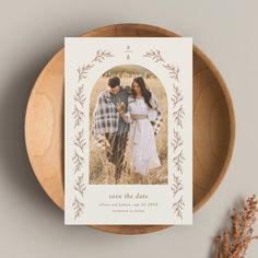 the save the date card is on top of a wooden plate next to dried flowers