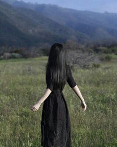 a woman in a black dress walking through tall grass