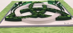 a green and white paper sculpture on top of a card board with ribbon around it