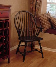 a wooden chair sitting in front of a window next to a dresser and wine rack