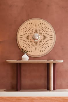 a vase sitting on top of a wooden table in front of a wall mounted circular mirror