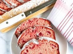 slices of strawberry pound cake on a plate next to a knife and cutting board with powdered sugar