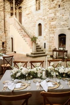 a table set up with place settings and flowers in front of an old stone building