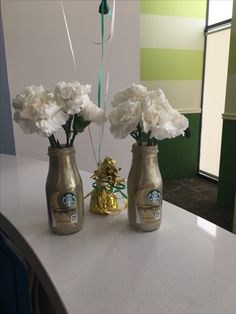 two vases with white flowers in them on a counter top next to each other