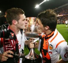 two men kissing each other with a trophy in front of them on a field at night