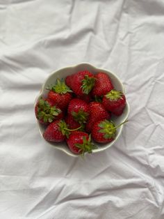 a bowl filled with strawberries on top of a white sheet