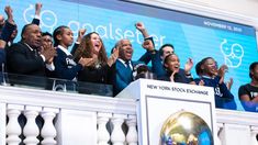 a group of people standing next to each other on top of a white fence with their hands in the air