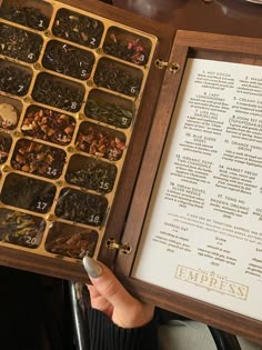 a person holding an open wooden box filled with different types of teas and numbers