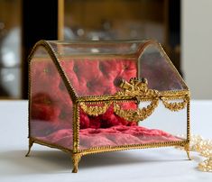 a glass box with red balls in it on a table next to pearls and a bead necklace