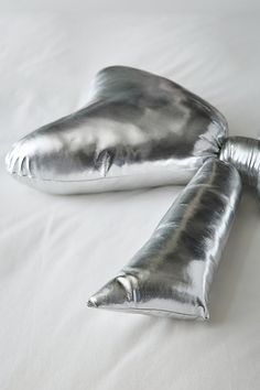 two shiny silver pillows laying on top of a white bed sheet with one pillow folded over the other