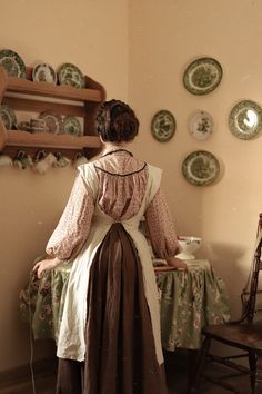 a woman standing in front of a table with plates on the wall behind her,