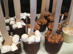 there are many desserts on the table with spoons sticking out of them and marshmallows