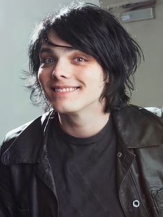 a young man with black hair wearing a leather jacket and smiling at the camera,