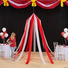 a woman standing in front of a red, white and yellow tent with balloons on it