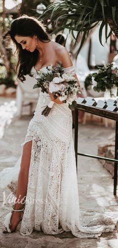 a woman in a white dress is standing near a table with flowers and greenery