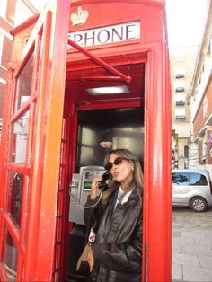 a woman standing in a red phone booth