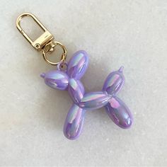 a purple balloon dog keychain on a white surface with a gold metal hook