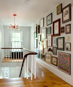 a staircase with many framed pictures on the wall and wood flooring, along with a chandelier