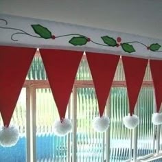 christmas decorations on the window sill in front of red and white curtains with pom - poms hanging from them