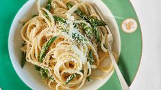 a green and white plate topped with pasta covered in parmesan cheese next to a fork