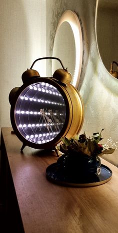 an alarm clock sitting on top of a wooden table next to a vase with flowers