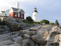 a lighthouse on top of a rocky hill next to a red building with white windows