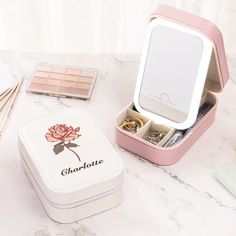 an open pink box with jewelry inside sitting on a marble table next to other items