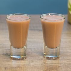 two shot glasses filled with liquid sitting on top of a wooden table next to an apple