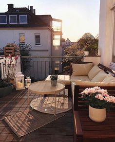 a balcony with couches, tables and potted flowers on the deck outside at sunset