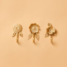 three gold flower brooches on a beige background