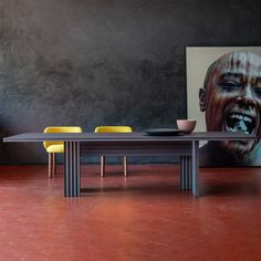 a dining table with two yellow chairs and a large painting on the wall behind it