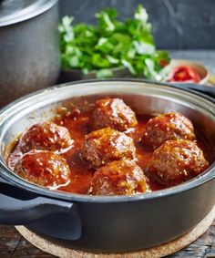 some meatballs are sitting in a pot on a wooden table next to other food