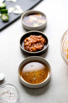 three bowls filled with food sitting on top of a counter next to other dishes and spoons