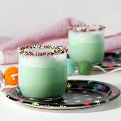 two glasses filled with green liquid and sprinkles sitting on top of a plate