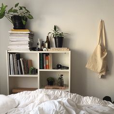 a bed with white sheets, bookshelf and plants on top of the bookcase