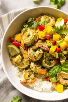 a white bowl filled with shrimp and veggies on top of rice next to cilantro