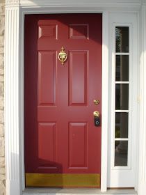 a red front door with gold trim and two sidelights on either side, next to a brick building