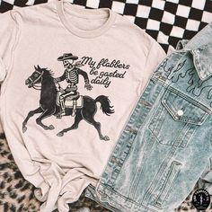 a white shirt with a skeleton riding a horse on it and an old jean jacket next to it